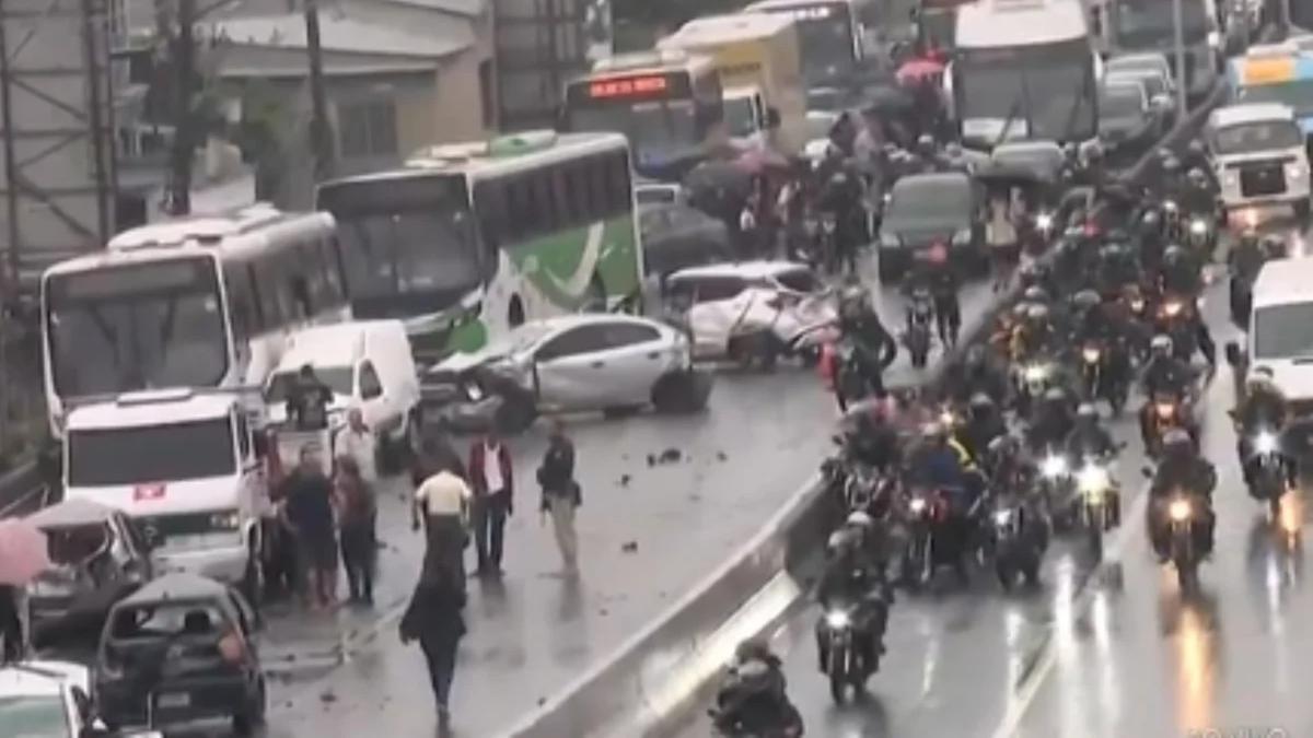 Carros danificados e ônibus ocupam a pista, enquanto motociclistas passam ao lado.