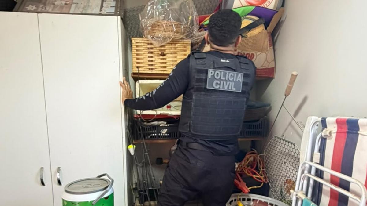 Policial de costas examina espaço com armário, cestos, cadeiras e utensílios domésticos.