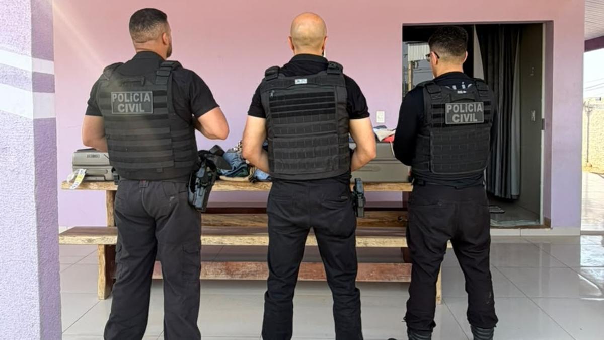 Três policiais civis de costas diante de uma mesa na varanda de uma residência.