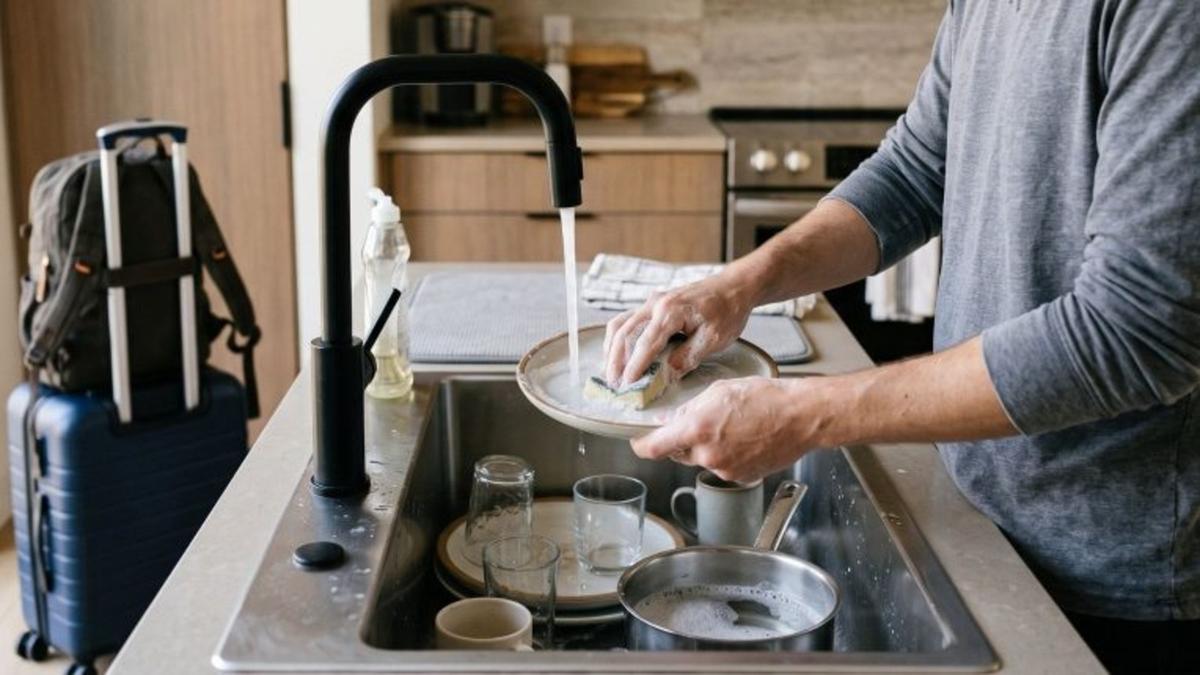 Pessoa lava louça em uma cozinha com a torneira aberta.